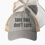 Gray and tan mesh back trucker hat with lake hair don’t care embroidered saying and black polka dot patterned underrim