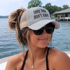 Woman wearing a light grey lake hair don’t care ponytail trucker hat on a boat at the lake during summer