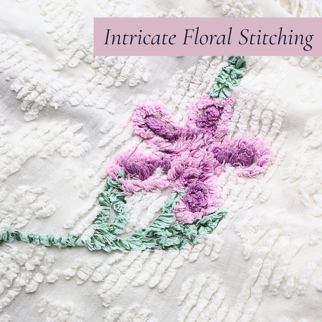 Close-up of the intricate lavender floral stitching on a vintage white chenille bedspread, showcasing dimensional tufting and classic craftsmanship. Perfect for cottage decor enthusiasts, farmhouse bedroom styling, vintage bedding collectors, and heirloom textile displays.