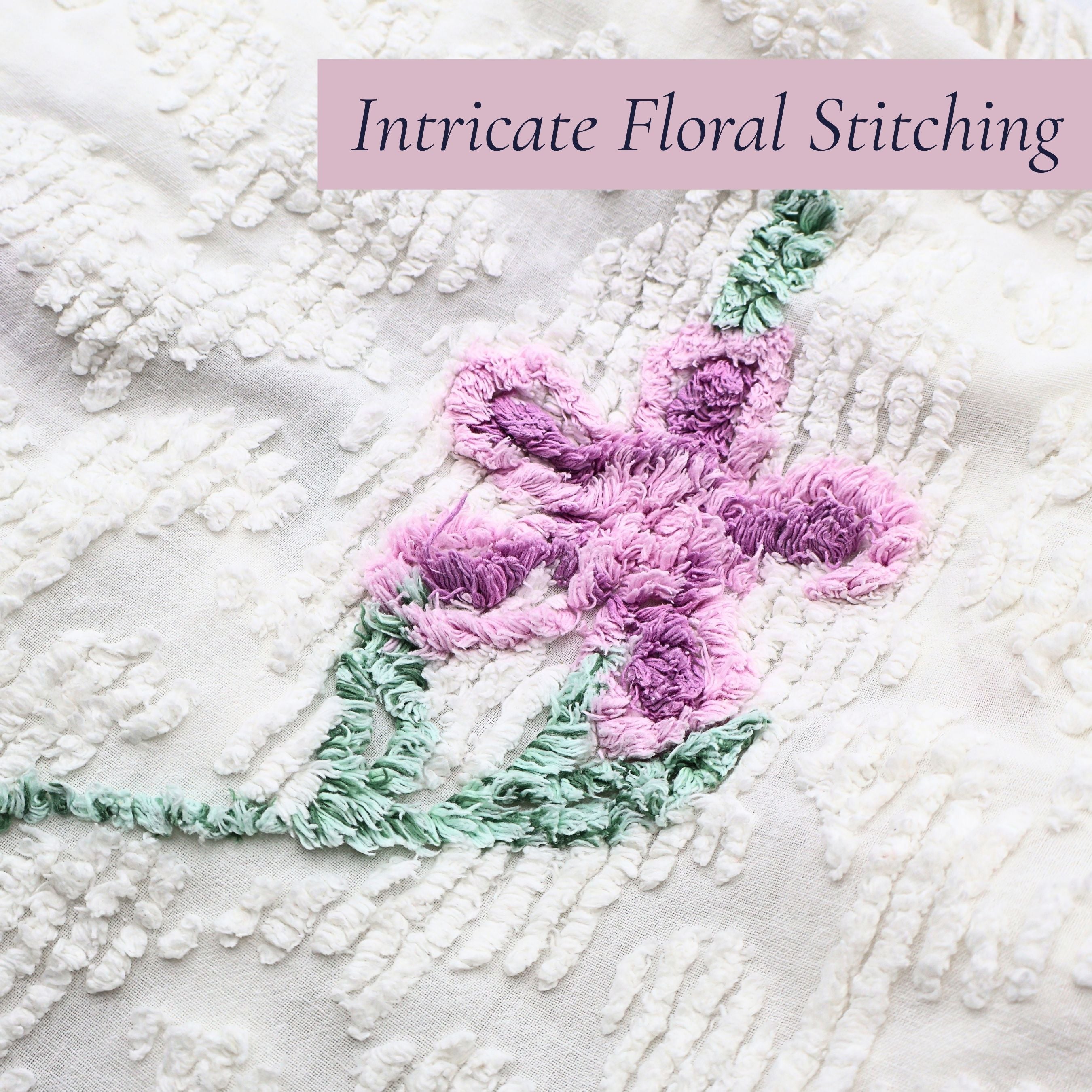 Close-up of the intricate lavender floral stitching on a vintage white chenille bedspread, showcasing dimensional tufting and classic craftsmanship. Perfect for cottage decor enthusiasts, farmhouse bedroom styling, vintage bedding collectors, and heirloom textile displays.
