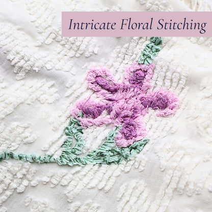 Close-up of the intricate lavender floral stitching on a vintage white chenille bedspread, showcasing dimensional tufting and classic craftsmanship. Perfect for cottage decor enthusiasts, farmhouse bedroom styling, vintage bedding collectors, and heirloom textile displays.