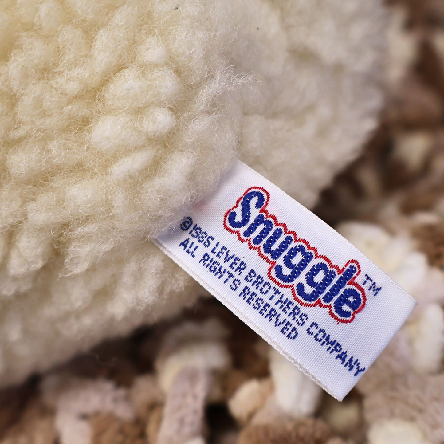 Rear view of a vintage 1986 Snuggle Bear displaying clean ivory plush and the original attached manufacturer tag. Ideal for collectors seeking authentic Lever Brothers advertising memorabilia, nostalgic plush toys, and vintage display pieces.
