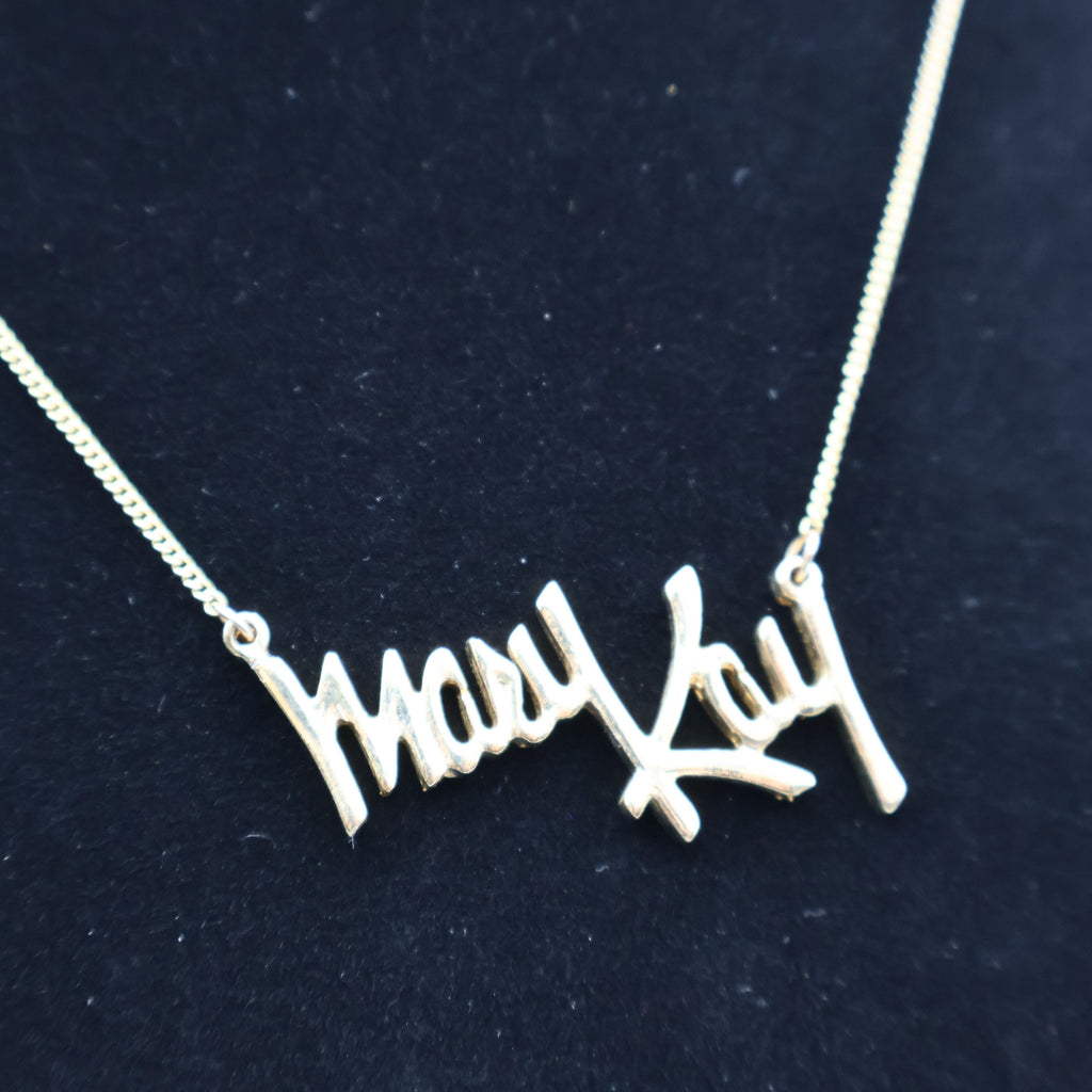 Close-up of vintage Mary Kay Lady gold script pendant necklace worn on display bust, collectible jewelry piece.