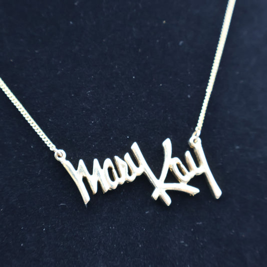 Close-up of vintage Mary Kay Lady gold script pendant necklace worn on display bust, collectible jewelry piece.