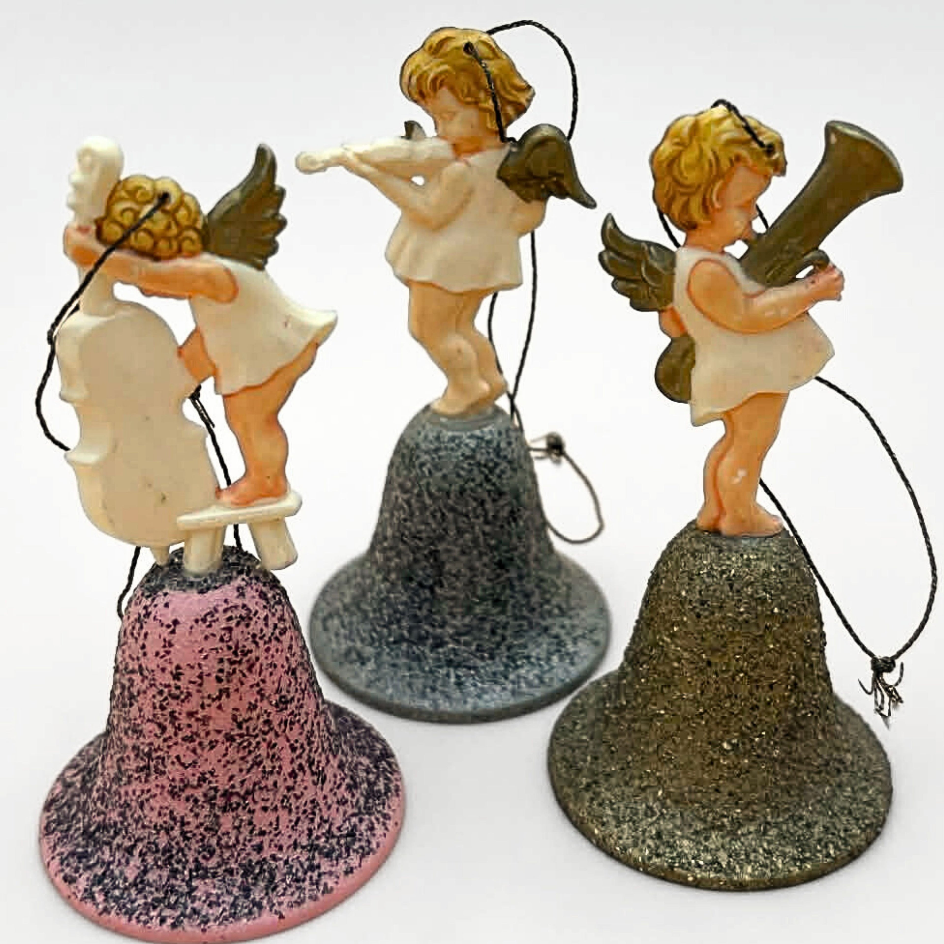 Angled perspective of vintage angel bell ornaments set featuring three musical cherubs on glitter bells. Instruments include cello, violin, and horn. Mid century West Germany Christmas decor with dimensional styling and vintage charm