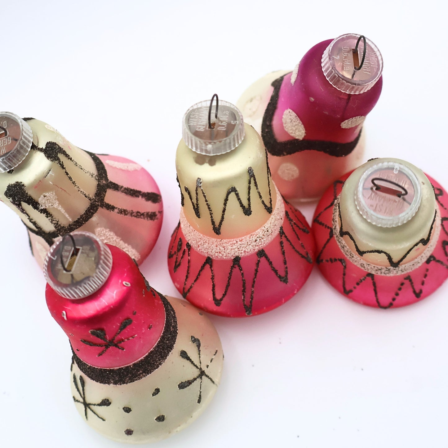 Top view of vintage West Germany bell ornaments featuring atomic black glitter detailing and pink mercury glass finishes