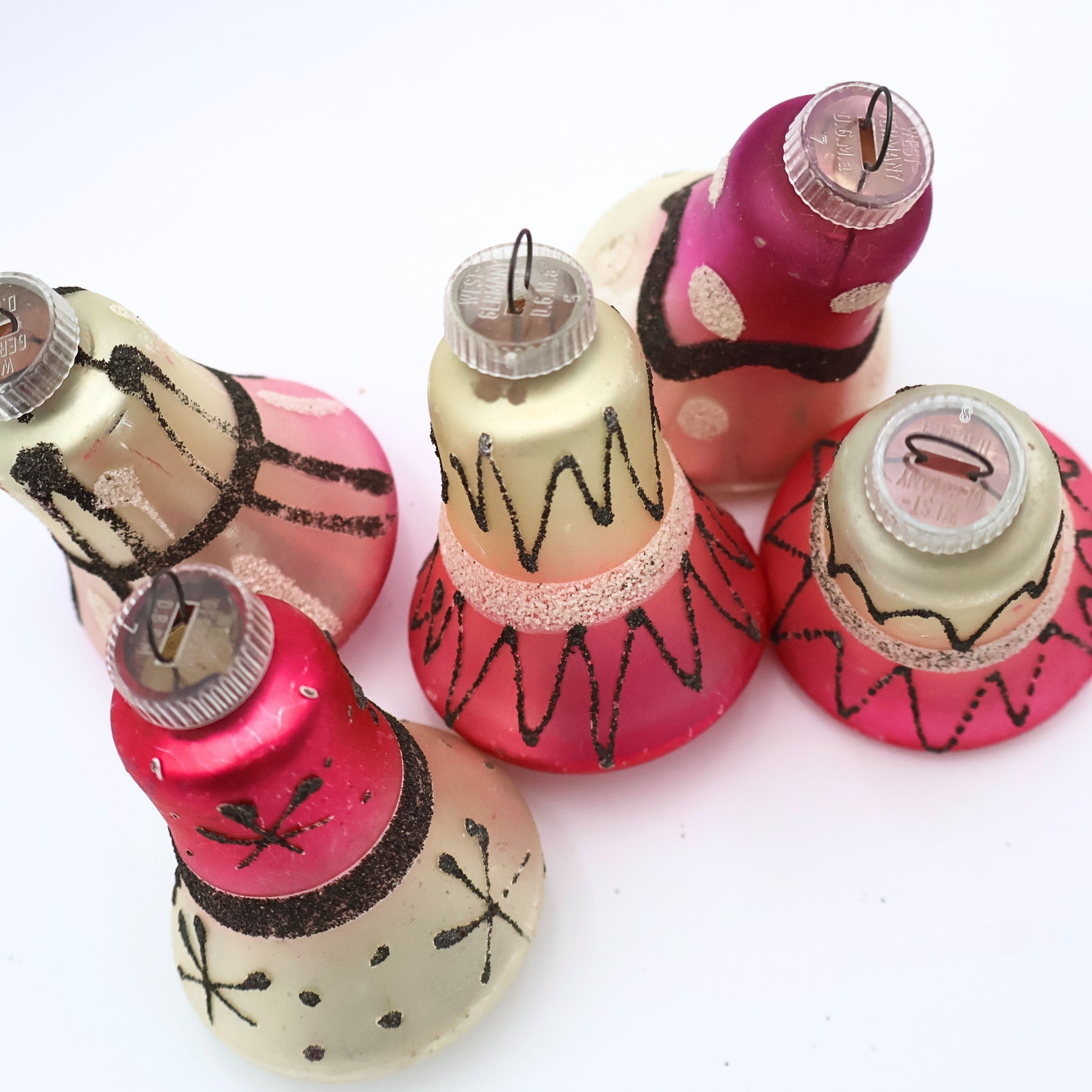 Top view of vintage West Germany bell ornaments featuring atomic black glitter detailing and pink mercury glass finishes