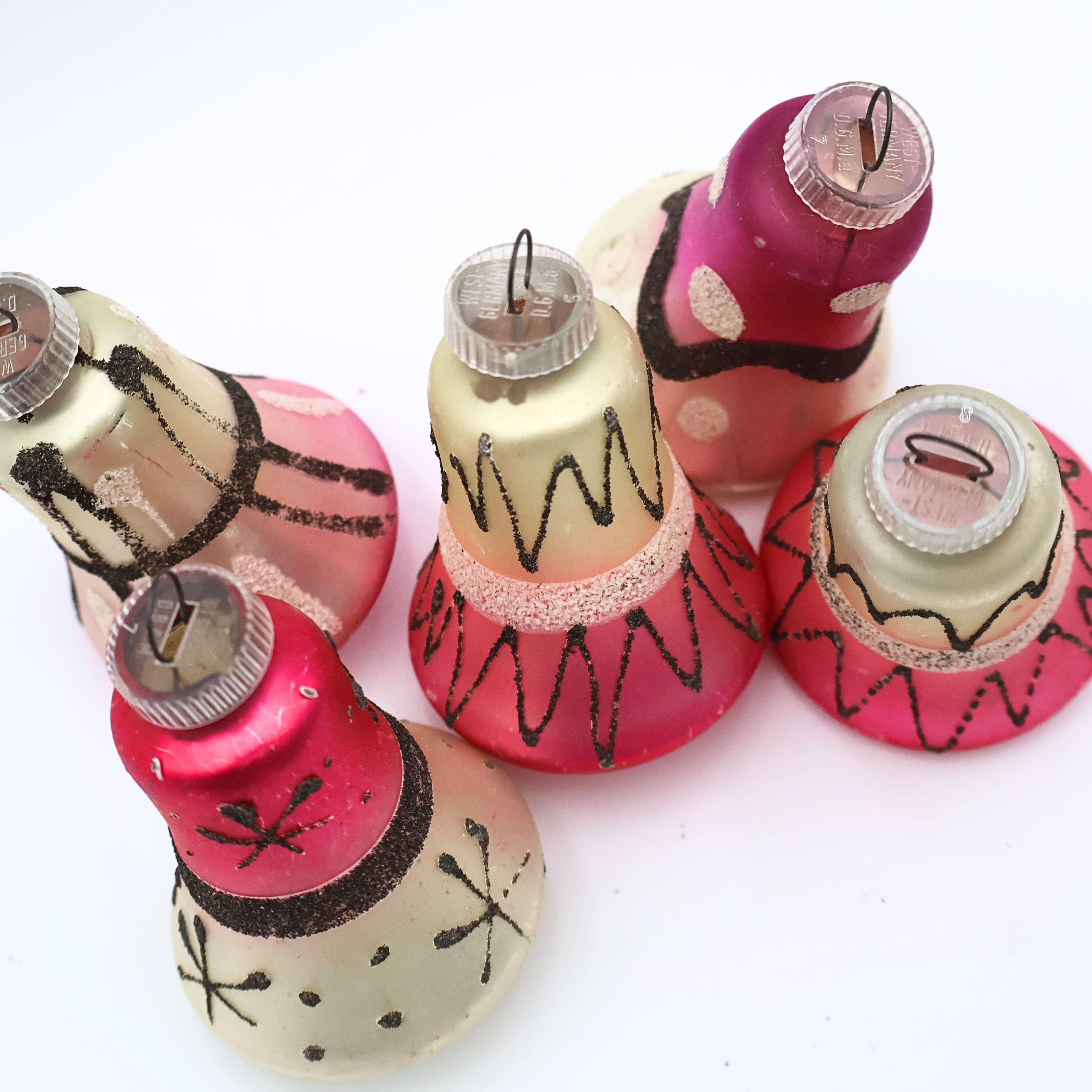 Top view of vintage West Germany bell ornaments featuring atomic black glitter detailing and pink mercury glass finishes