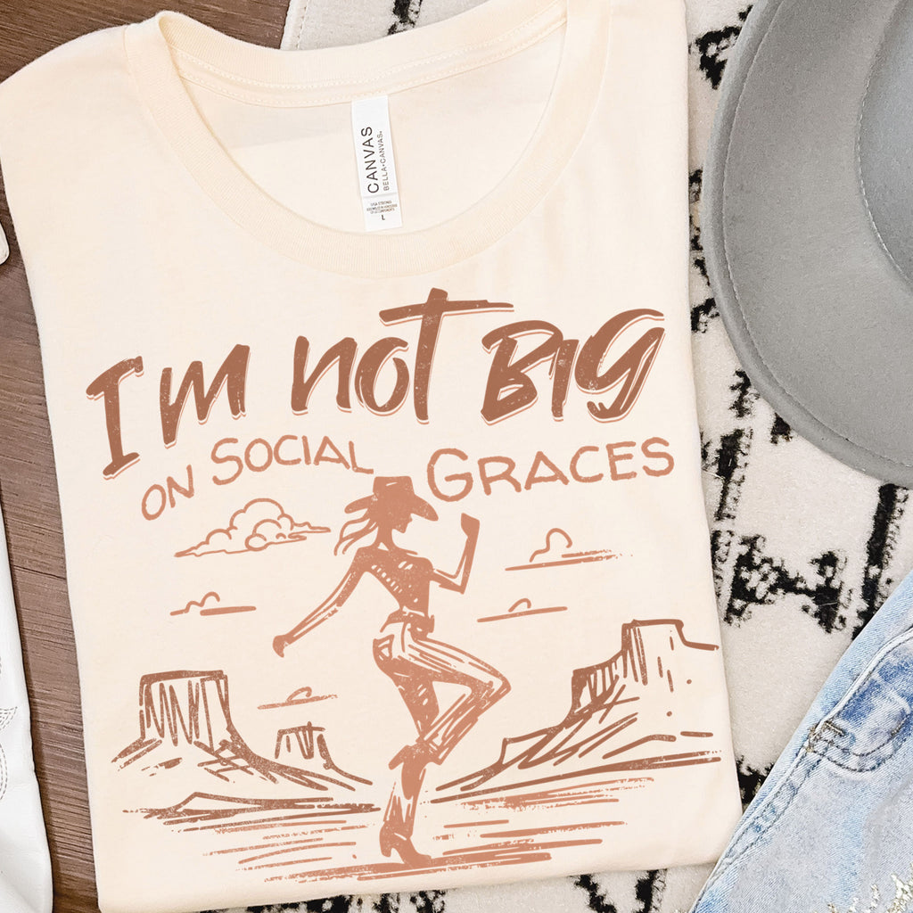 Neutral cream western graphic tee folded in flat lay with cowgirl design and desert illustration, boutique t-shirt styled with western accessories