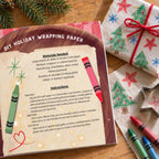 DIY holiday wrapping paper activity from Oliver the Owl: A Sweet Season beside crayons, a star cookie cutter and a gift wrapped in paper decorated with colorful Christmas trees, stars and snowflakes.