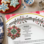 Sweet Snowflake Sugar Cookies recipe from Oliver the Owl: A Sweet Season beside blue and white iced snowflake cookies on a red plate, with sprinkles and cookie cutters nearby.