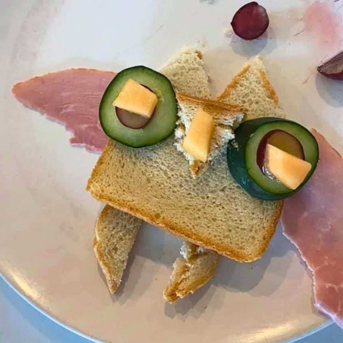 Homemade owl-shaped sandwich inspired by Oliver the Owl: The Culinary Pro, arranged on a plate with cucumber and cheese eyes, a cheese beak, bread ears and triangular ham wings.