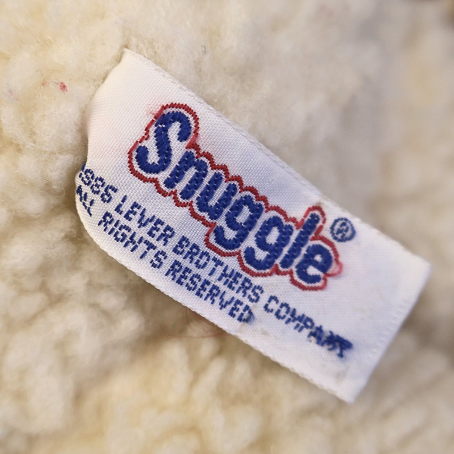 Close-up of the original Snuggle by Lever Brothers fabric tag attached to this authentic 1986 plush mascot. The clear copyright label adds collector appeal and confirms its vintage advertising heritage, making it desirable for retro memorabilia and nostalgic toy collections.