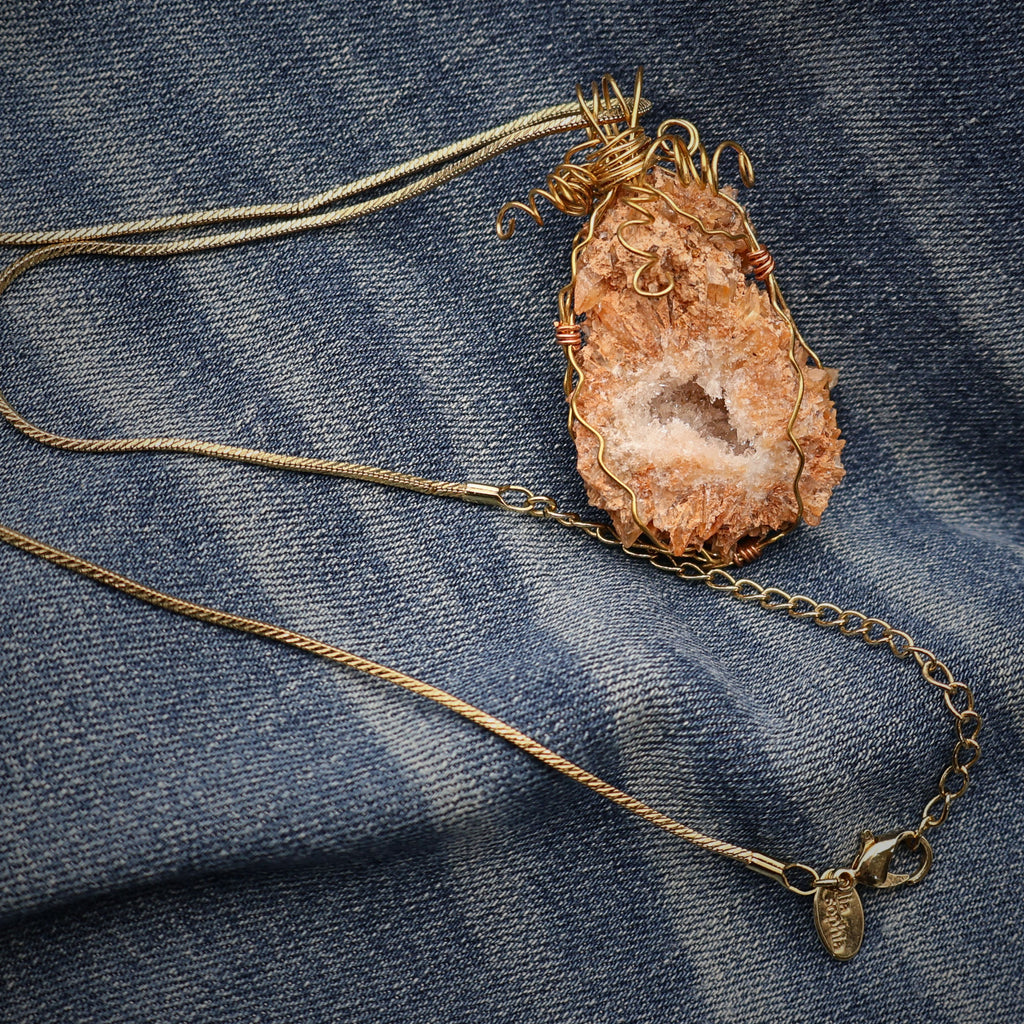 Peach druzy quartz geode necklace displayed flat on denim showing full gold chain, adjustable length design with lobster clasp closure, handmade crystal pendant necklace with boho western styling and natural stone jewelry details