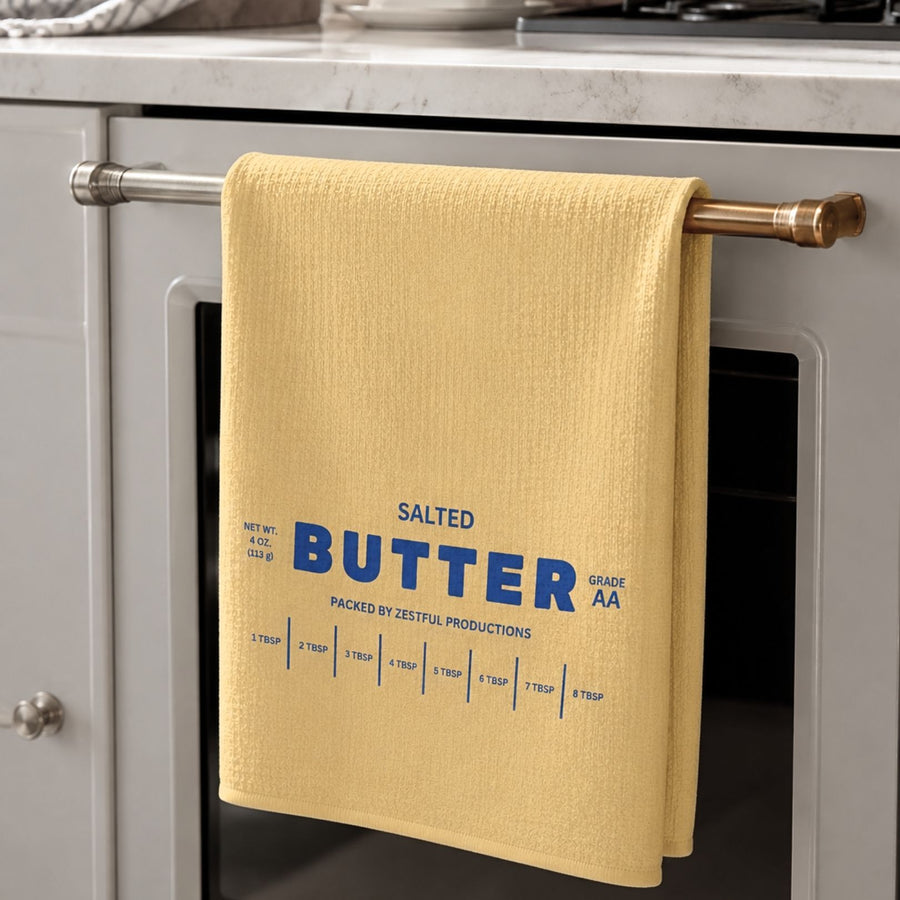 Personalized salted butter microfiber tea towel hanging on oven handle in neutral modern kitchen with blue butter wrapper inspired typography and tablespoon measurement markings. Funny baker gift dish cloth for chefs, cooking lovers and quirky kitchen decor enthusiasts.