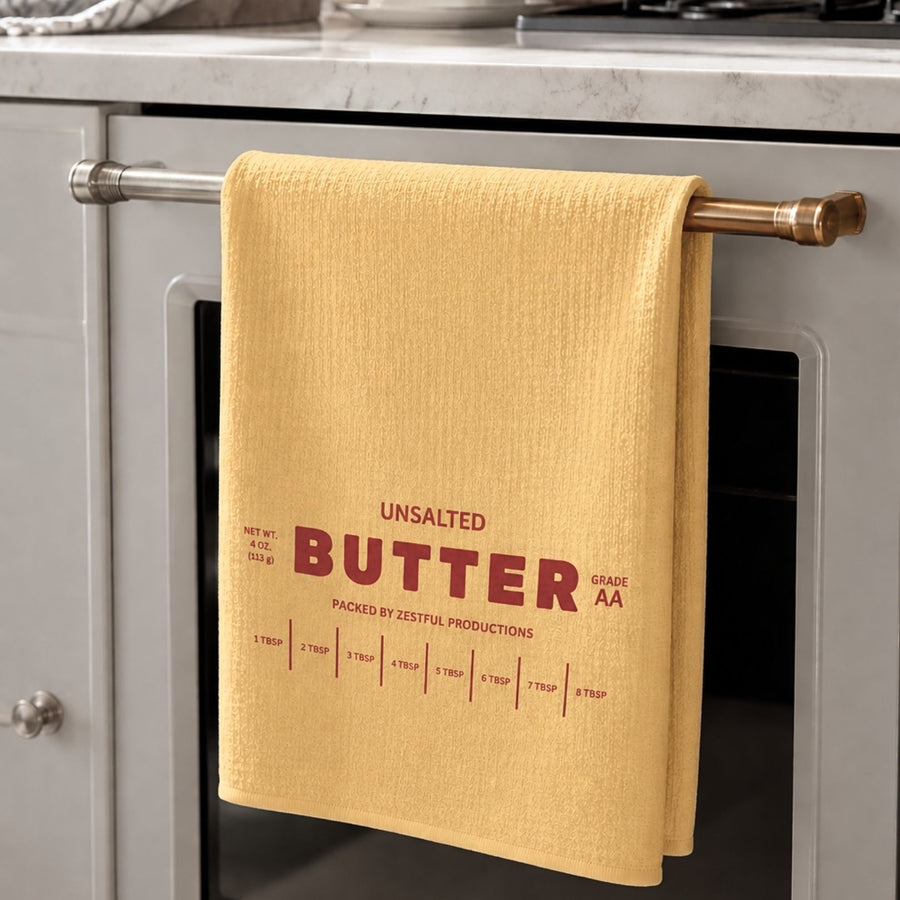 Personalized unsalted butter microfiber tea towel hanging on oven handle in modern neutral kitchen with red butter wrapper inspired typography and tablespoon measurement markings. Funny baker gift dish cloth for chefs, cooking lovers and quirky kitchen decor enthusiasts.