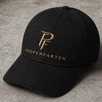 Black Poopenfarten Motorwerke dad cap with gold embroidered PF logo photographed on a concrete surface in a luxury automotive-inspired streetwear setting.