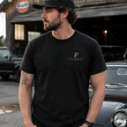 Man wearing black Poopenfarten Motorwerke automotive humor t-shirt with minimalist PF chest logo in vintage garage environment.