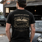 Man wearing black Poopenfarten Motorwerke funny car shirt featuring vintage racing back graphic with sports car and checkered flags in garage setting.