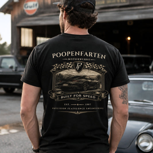 Man wearing black Poopenfarten Motorwerke funny car shirt featuring vintage racing back graphic with sports car and checkered flags in garage setting.
