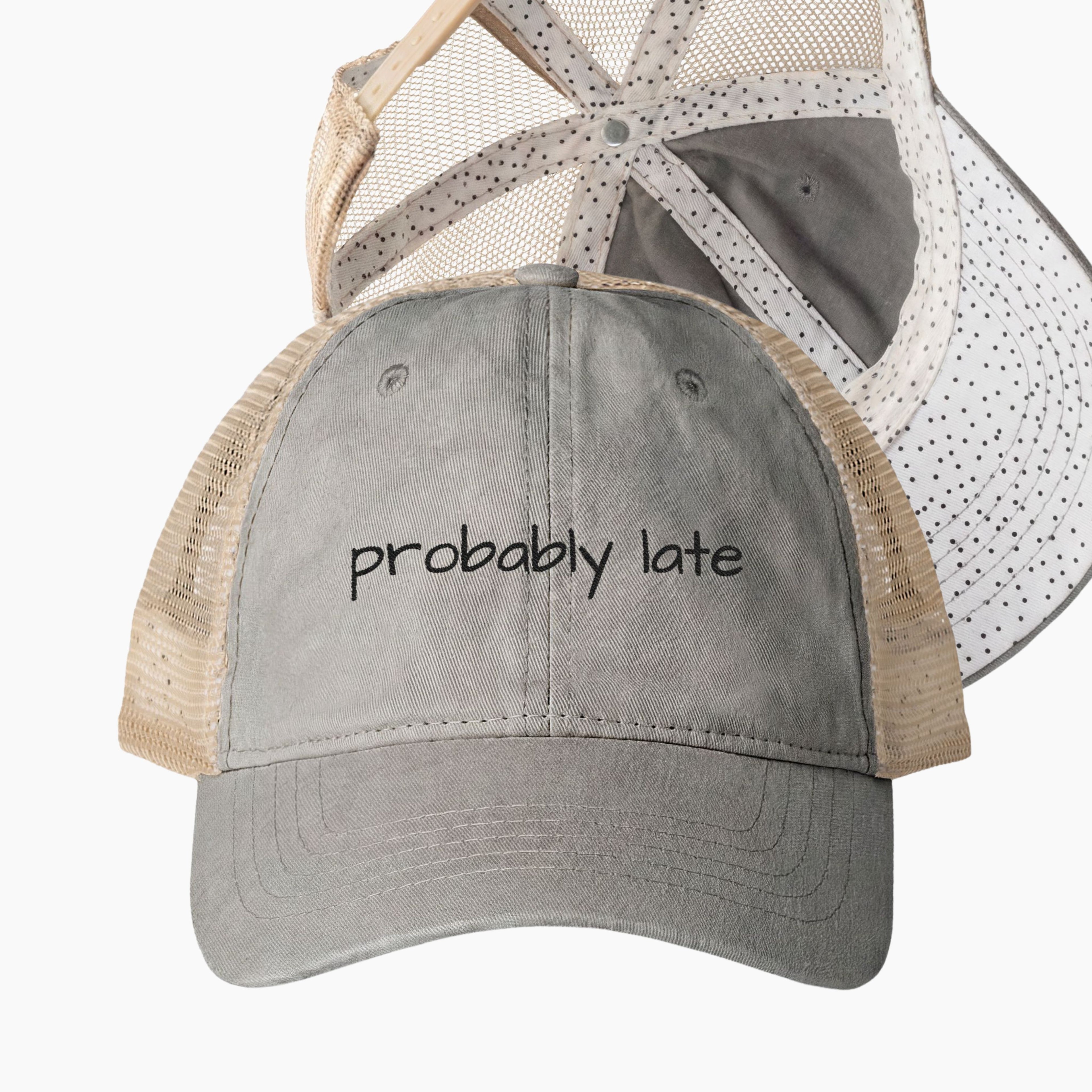 Gray and tan mesh back trucker hat with probably late embroidered saying and black polka dot patterned underrim