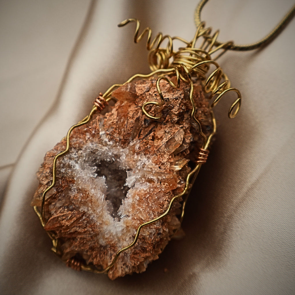 Close-up of raw druzy quartz geode pendant with gold wire wrapping, highlighting crystal cluster formation and natural peach tones, handmade statement necklace featuring mineral specimen detail and boho western jewelry aesthetic