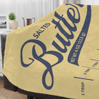 Salted butter minky throw blanket draped over a couch with yellow butter label design and blue script lettering. Soft cozy blanket for living room decor, lounging, and butter lover gifts.