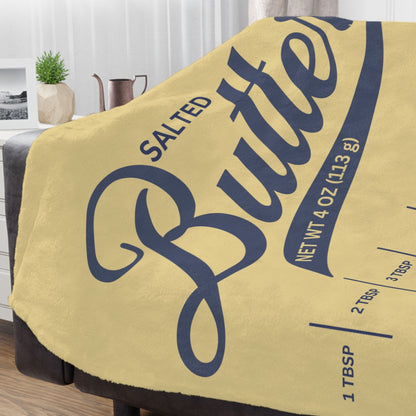 Salted butter minky throw blanket draped over a couch with yellow butter label design and blue script lettering. Soft cozy blanket for living room decor, lounging, and butter lover gifts.