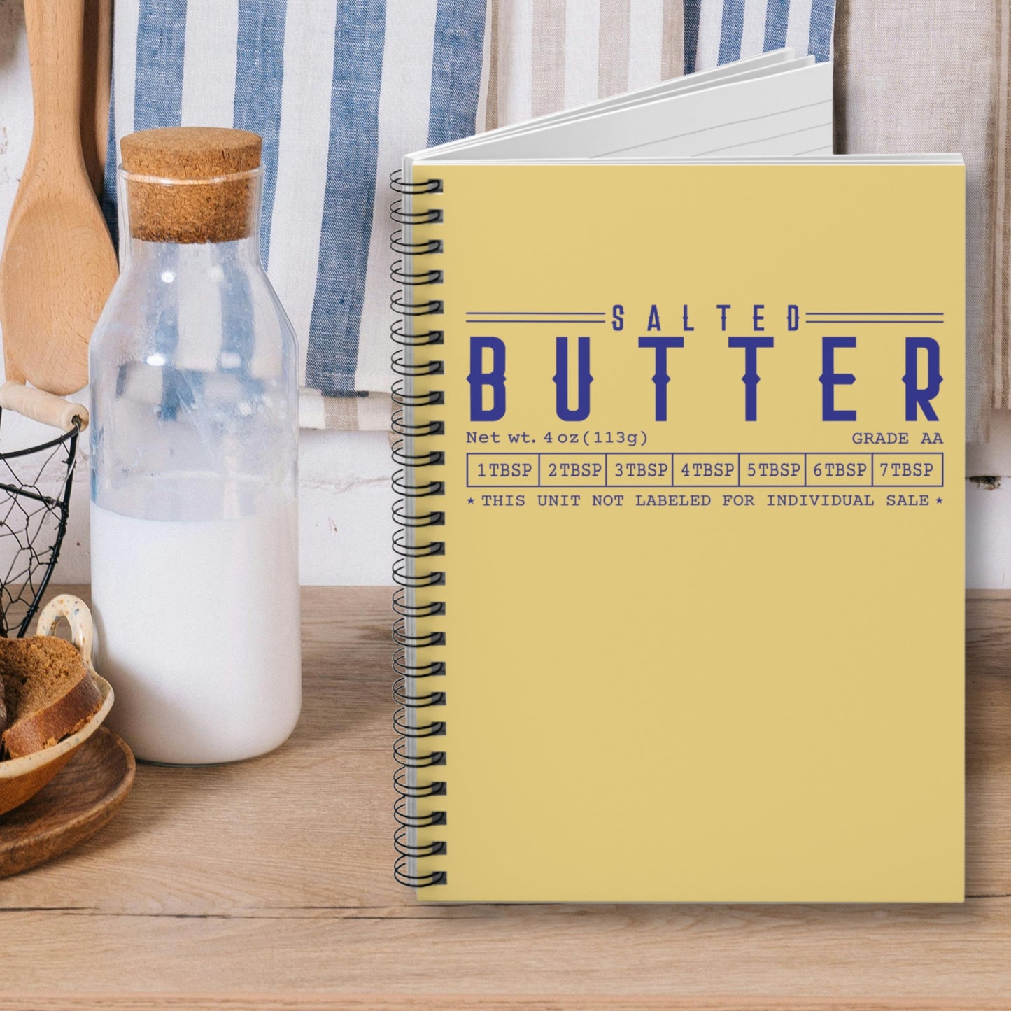 Salted butter notebook with yellow cover and blue lettering displayed on kitchen counter. Spiral journal for notes, lists, and everyday writing with bold design.