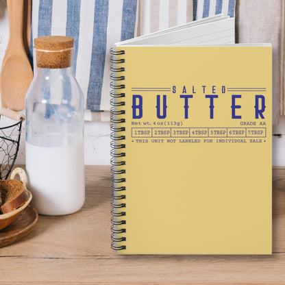 Salted butter notebook with yellow cover and blue lettering displayed on kitchen counter. Spiral journal for notes, lists, and everyday writing with bold design.