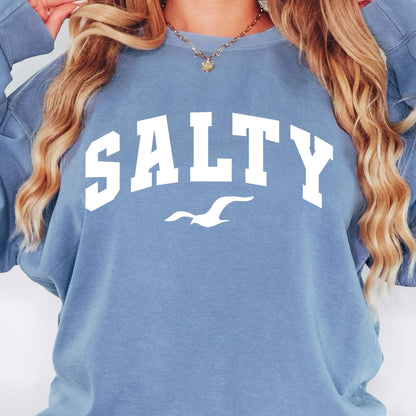 Woman wearing blue jean SALTY sweatshirt, oversized beach crewneck, relaxed coastal outfit, casual seaside fashion, comfortable vacation clothing for women, nautical graphic sweatshirt