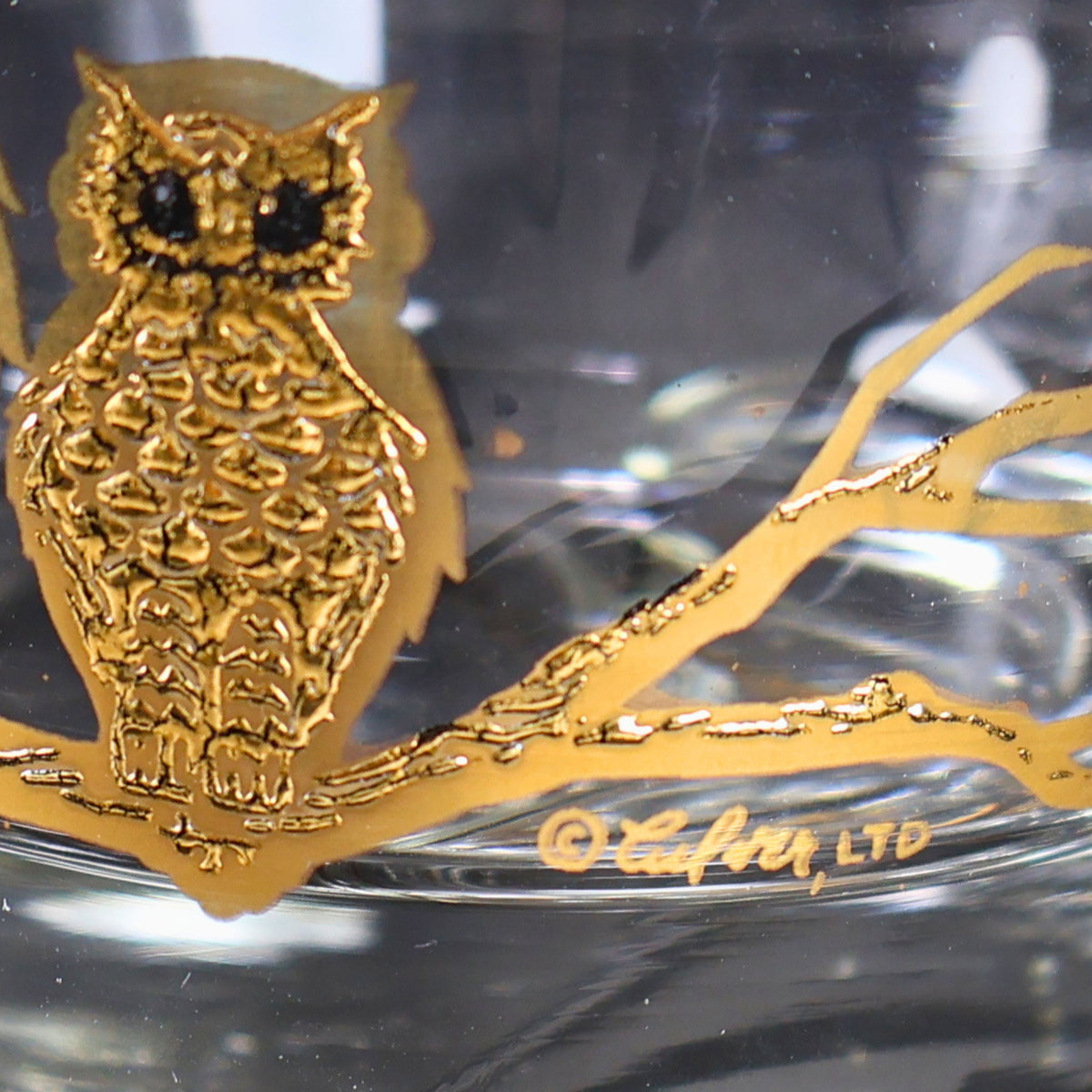 Detailed view of the smaller textured gold owl perched on a branch beside the gold Culver Ltd. signature. The photograph shows the owl’s dark eye accents, layered feather pattern, metallic branchwork, and clear glass background at close range.