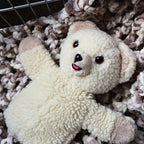 Vintage 1986 Snuggle Bear hand puppet by Lever Brothers shown from the front on a soft textured blanket. This classic cream plush advertising mascot features an embroidered smile, original design details, and makes a charming collectible for laundry room decor or nostalgic vintage toy displays.