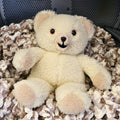 Vintage 1986 Snuggle Bear by Lever Brothers Company sitting on a cozy knit blanket. This original 15-inch advertising mascot features soft ivory sherpa plush, original tags, and a friendly smiling face, making it a charming collectible for nostalgic home decor, vintage plush collections, and childhood memory displays.