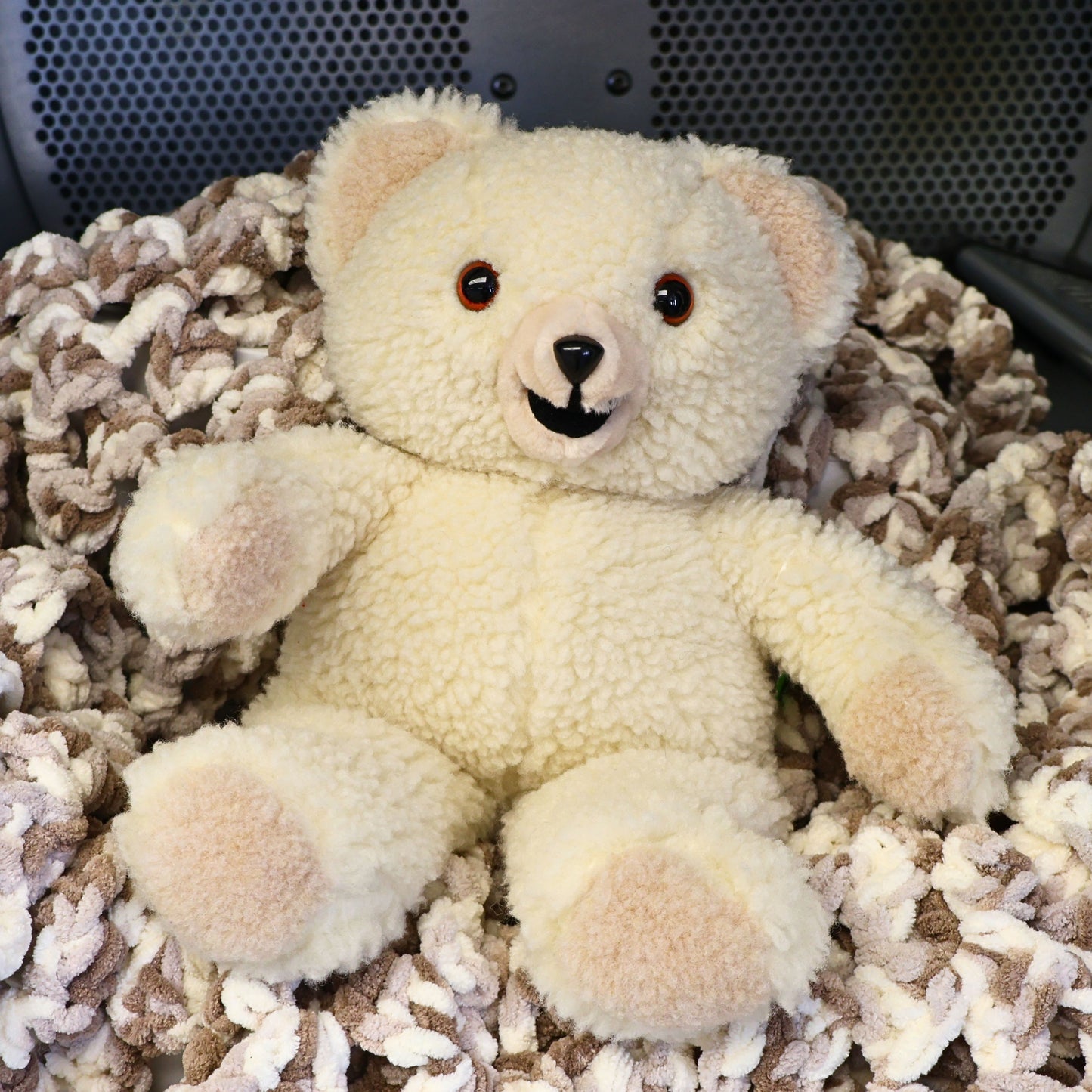 Vintage 1986 Snuggle Bear by Lever Brothers Company sitting on a cozy knit blanket. This original 15-inch advertising mascot features soft ivory sherpa plush, original tags, and a friendly smiling face, making it a charming collectible for nostalgic home decor, vintage plush collections, and childhood memory displays.