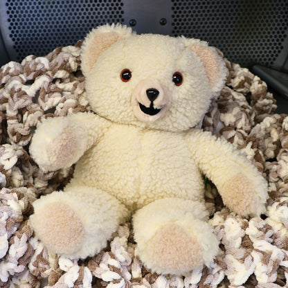 Vintage 1986 Snuggle Bear by Lever Brothers Company sitting on a cozy knit blanket. This original 15-inch advertising mascot features soft ivory sherpa plush, original tags, and a friendly smiling face, making it a charming collectible for nostalgic home decor, vintage plush collections, and childhood memory displays.