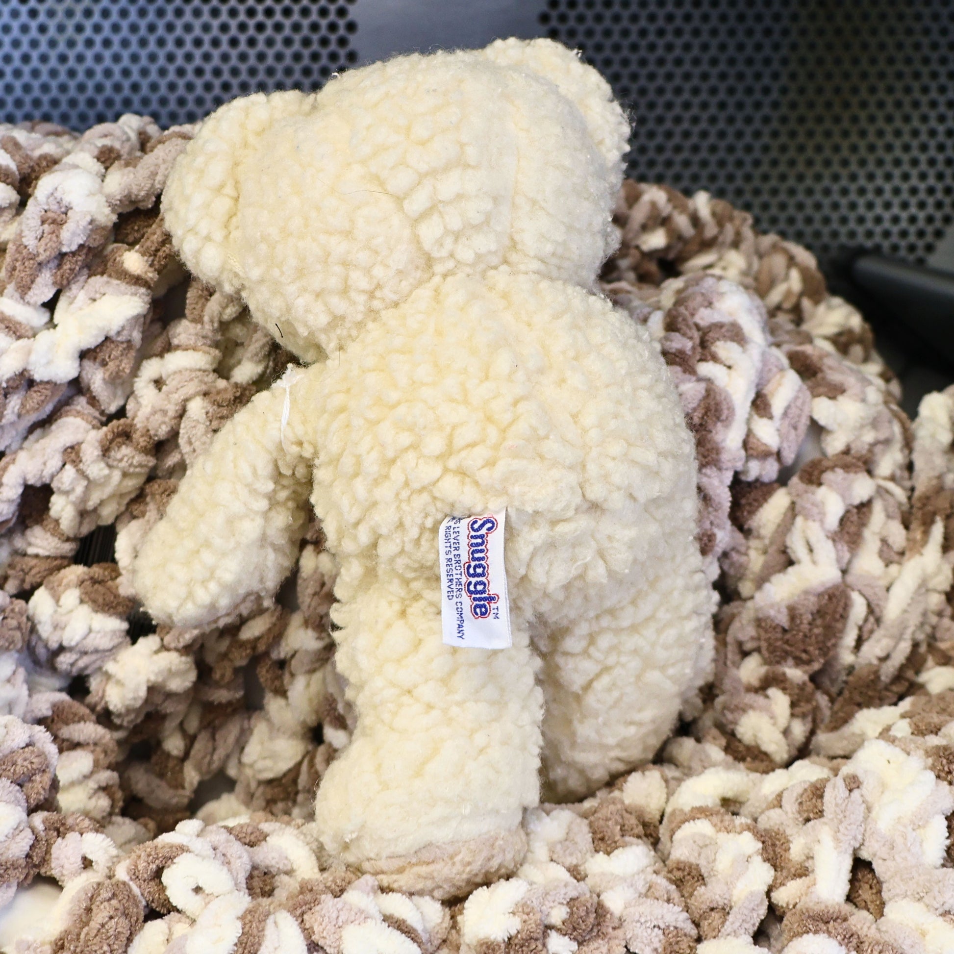Rear view of a vintage 1986 Snuggle Bear plush featuring the original sewn-in Snuggle copyright tag. The fluffy cream plush and authentic label make this advertising mascot an appealing collectible for vintage decor, laundry room displays, and nostalgic toy collections.