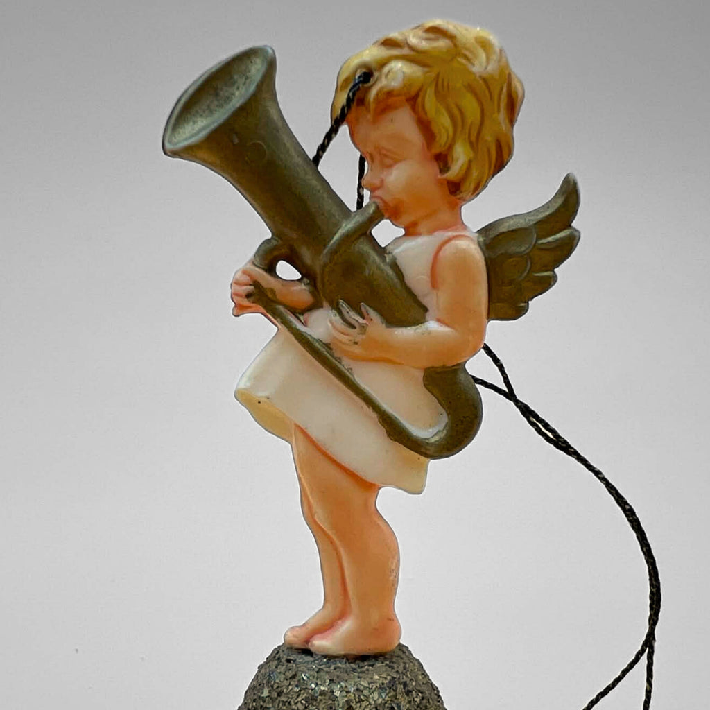 Single vintage angel bell ornament featuring cherub playing a horn instrument standing on a gold glitter bell. Side profile shows wing detail and hanging string. Mid century West Germany Christmas ornament collectible