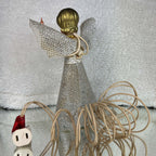 Rear view of the vintage angel tree topper, showing gold-colored molded hair, silver mesh wings, and a long flared mesh skirt. Ivory-colored wires run down the back and coil beside the figure, with a pale electrical fitting and red paper tag visible at the left.