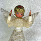Upper front view of a vintage Christmas angel tree topper against a pale textured background. Gold-colored curls and a red bow frame her painted face, while raised amber candle bulbs, silver mesh wings, a cream textured bodice, and metallic waist trim are visible.
