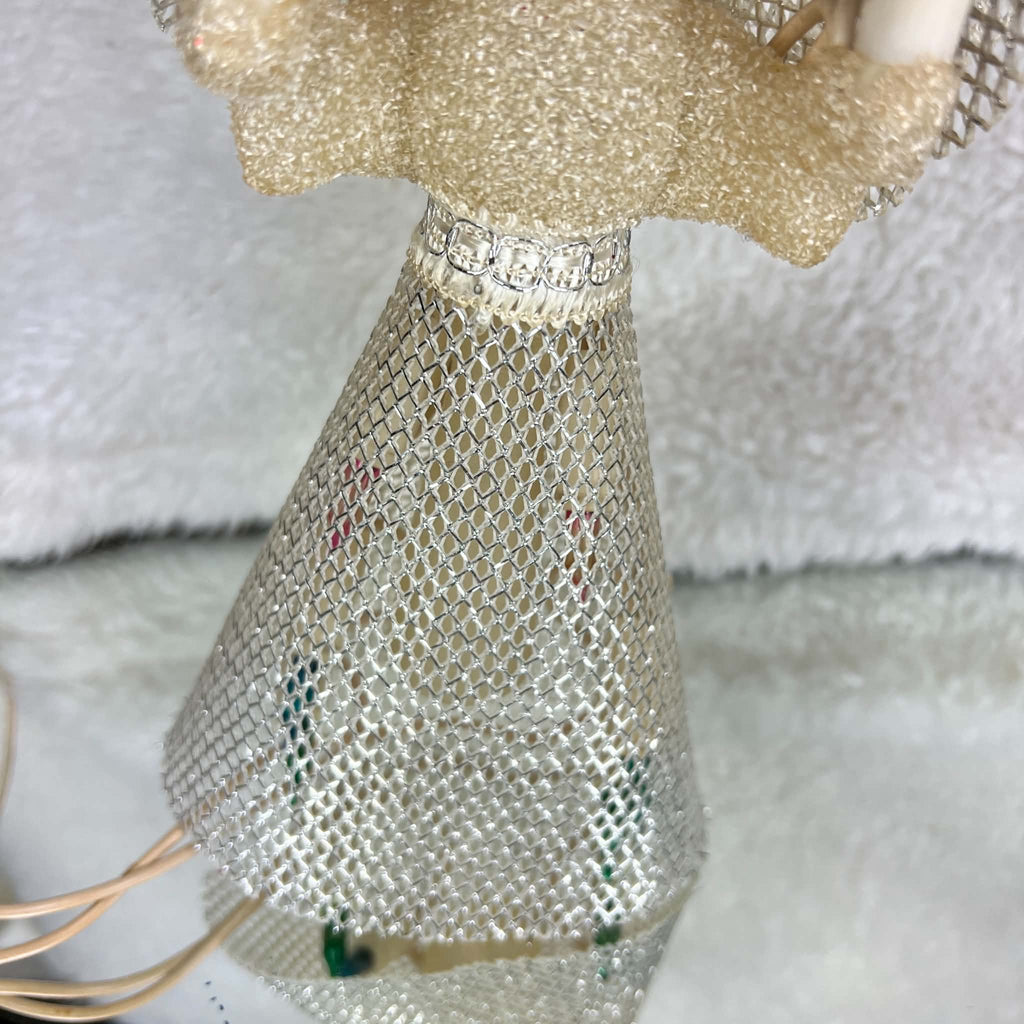 Front detail of a vintage lighted angel tree topper’s flared silver mesh skirt beneath a cream textured bodice and metallic waist trim. Colored bulbs and pale sockets are visible through the open mesh, with ivory-colored cord resting beside the skirt on a light surface.