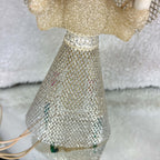 Front detail of a vintage lighted angel tree topper’s flared silver mesh skirt beneath a cream textured bodice and metallic waist trim. Colored bulbs and pale sockets are visible through the open mesh, with ivory-colored cord resting beside the skirt on a light surface.