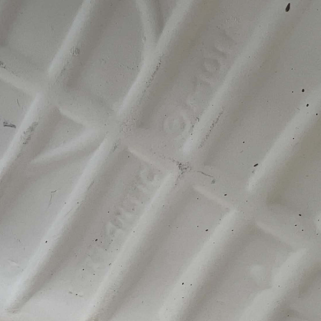 Close-up of the underside of an ivory ceramic boot planter, photographed to show the extremely faint impressed lettering believed to read Atlantic Mold. Surface texture, small dark specks and subtle marks are visible around the difficult-to-read maker’s impression.
