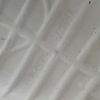 Close-up of the underside of an ivory ceramic boot planter, photographed to show the extremely faint impressed lettering believed to read Atlantic Mold. Surface texture, small dark specks and subtle marks are visible around the difficult-to-read maker’s impression.