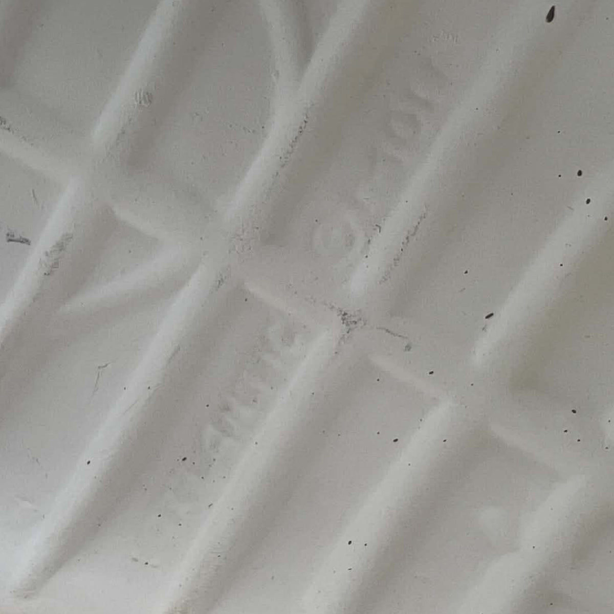 Close-up of the underside of an ivory ceramic boot planter, photographed to show the extremely faint impressed lettering believed to read Atlantic Mold. Surface texture, small dark specks and subtle marks are visible around the difficult-to-read maker’s impression.