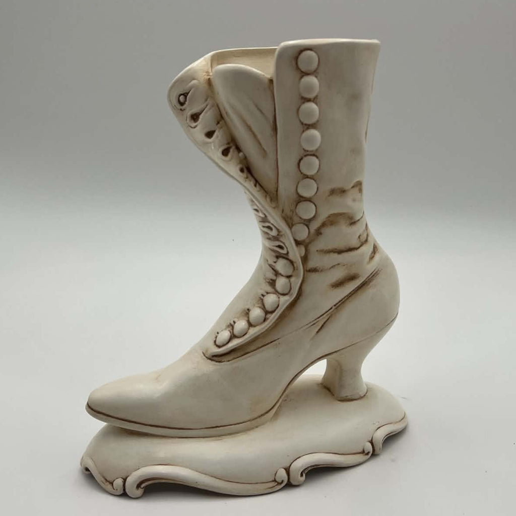 Vintage Atlantic Mold ceramic planter shown in profile as an ivory Victorian high-button boot. Raised round buttons follow the curved front panel, with brown antiquing defining the folds, seams, slender heel and scrolling pedestal base against a neutral background.