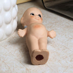 Bottom view of the vintage bisque Kewpie doll lying flat to display the hollow vent opening underneath, molded feet, rounded body, and painted facial details while documenting the underside condition.