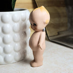Right side profile of the vintage bisque Kewpie figurine featuring its smiling expression, rounded body, painted hair accents, and molded hands. The photograph highlights the doll's charming proportions and vintage craftsmanship.