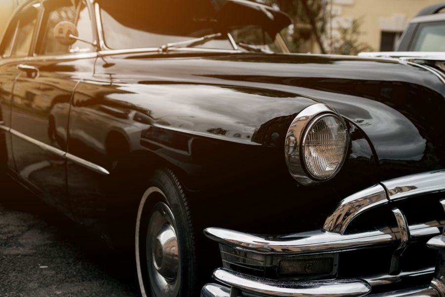 Close-up of a vintage black classic car with chrome detailing and headlight, used as a background for men’s fashion and vintage style collection, conveying timeless, rugged aesthetic