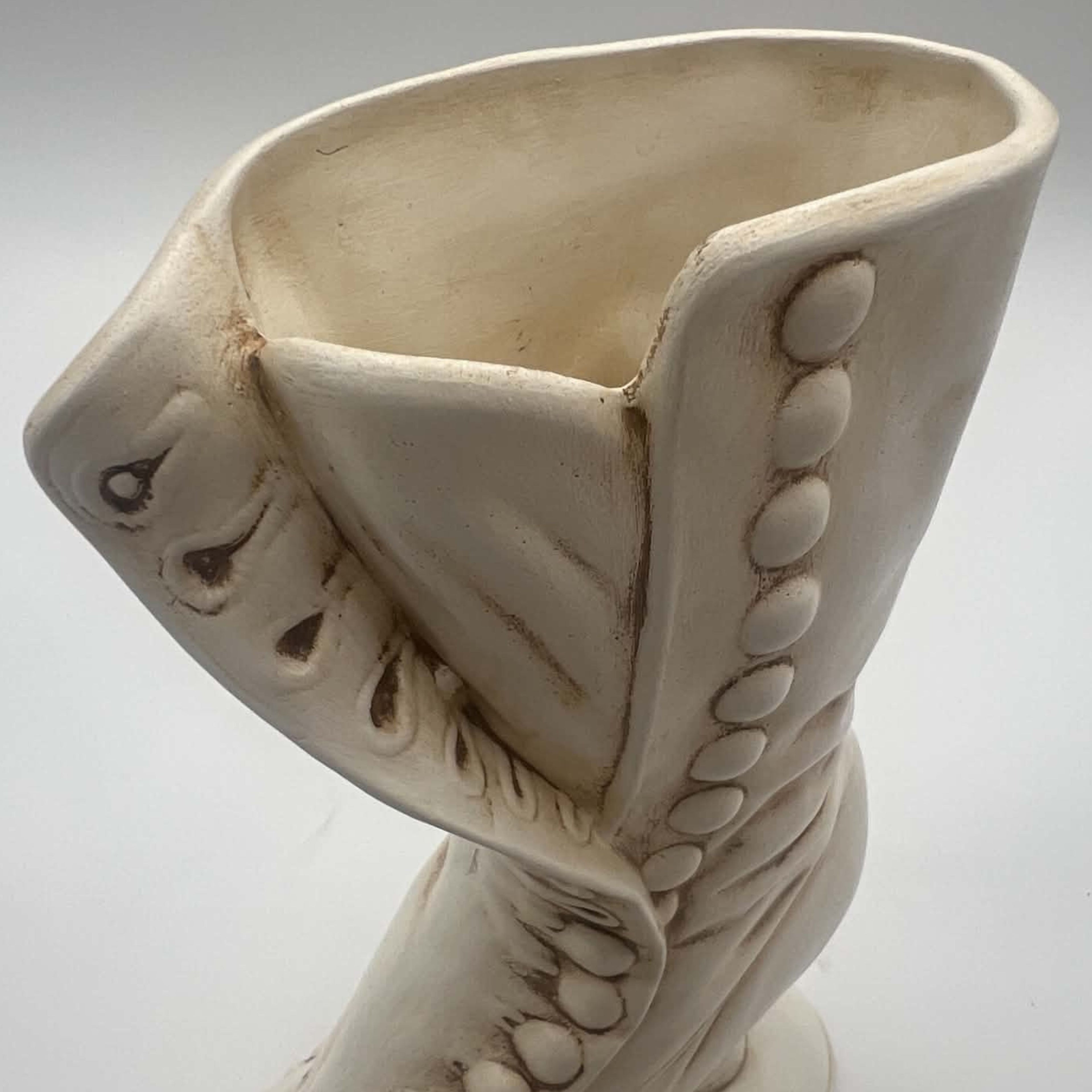 Close view of the open upper portion of an ivory Victorian boot planter, including its curved rim, folded ceramic flap and vertical row of raised buttons. Brown antiquing emphasizes the sculpted folds, button edges and pierced ornamental details near the front opening.